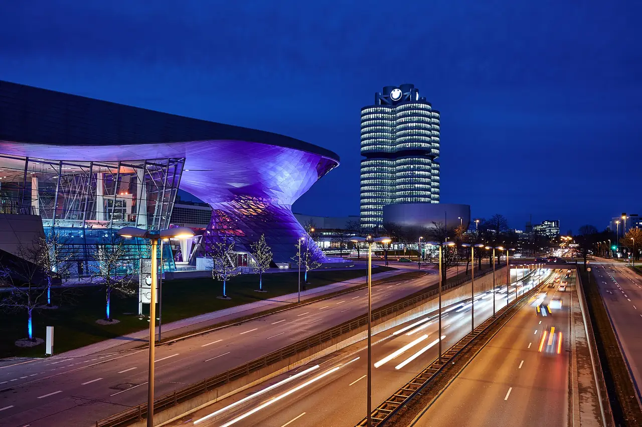 BMW Welt ส่องไฟสีม่วงยามค่ำ ข้างตึก BMW Vierzylinder ภาพจาก Wikimedia Commons ผู้ถ่าย Steffen Flor สัญญา CC BY-SA 2.0 ชื่อไฟล์ระบุธันวาคม 2564