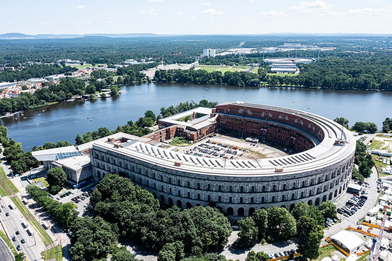 อาคาร Kongresshalle ที่สร้างไม่เสร็จริมทะเลสาบ Dutzendteich มองจากมุมสูง ภาพจาก Wikimedia Commons ผู้ถ่าย Kasa Fue สัญญา CC BY-SA 4.0 ถ่ายกรกฎาคม 2564 ปัจจุบันมีงานก่อสร้างในลานด้านใน