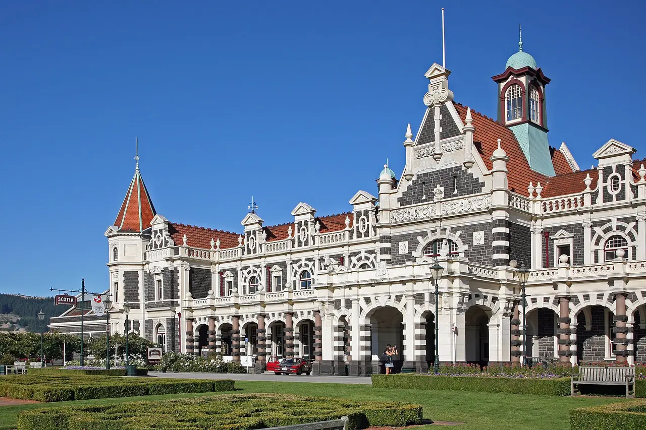 ด้านหน้าสถานีรถไฟ Dunedin หินสองสีและหลังคากระเบื้องส้ม ภาพจาก Wikimedia Commons ผู้ถ่าย W. Bulach สัญญา CC BY-SA 4.0 ไม่ระบุปีที่ถ่าย