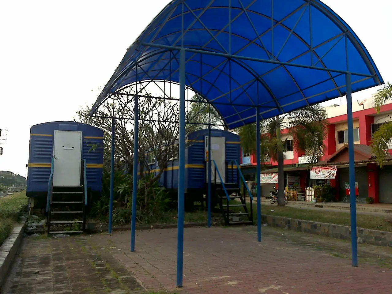 ตู้โดยสารรถไฟสีน้ำเงินจอดใต้หลังคาโค้งข้างสถานี ชื่อไฟล์บนคอมมอนส์เรียกว่าห้องสมุดรถไฟบุรีรัมย์ ภาพจาก Wikimedia Commons ผู้ถ่าย Mr.BuriramCN สัญญา CC BY-SA 3.0 เป็นภาพเก่า ไม่ยืนยันว่ายังเปิดให้ใช้