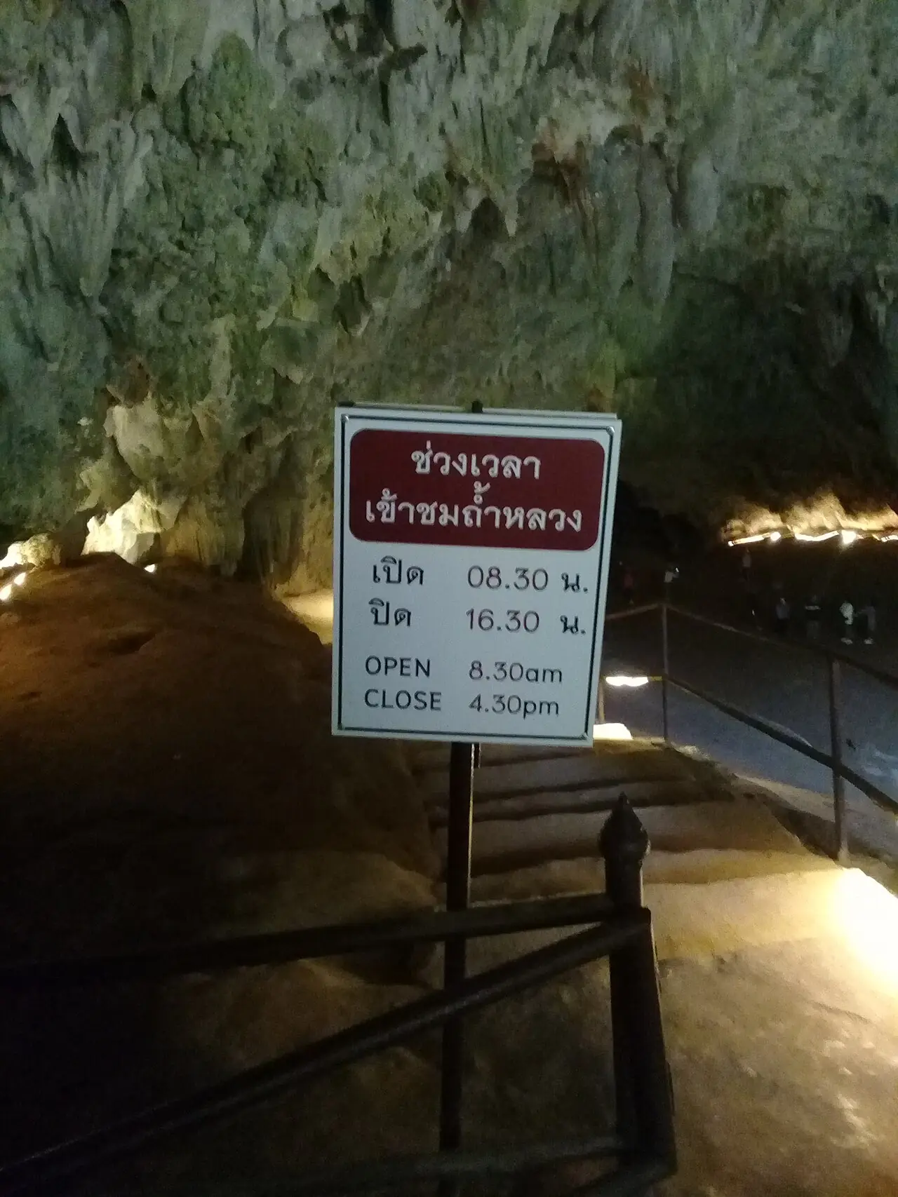 ป้ายช่วงเวลาเข้าชมถ้ำหลวง เปิด 08.30 น. ปิด 16.30 น. เป็นภาษาไทยและอังกฤษ ติดอยู่ในโถงถ้ำที่มีหินงอกหินย้อย ภาพจาก Wikimedia Commons ผู้ถ่าย Taweetham สัญญา CC BY-SA 4.0 ข้อมูลไฟล์ลงวันที่ถ่าย 20 ม.ค. 2566 จึงอาจไม่ใช่เวลาปัจจุบัน