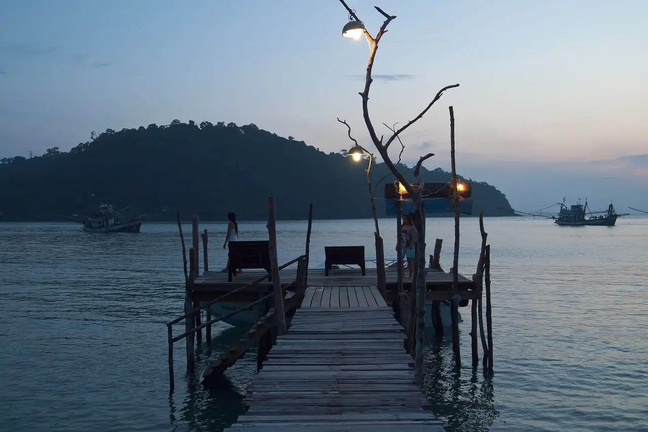สะพานไม้ยามเย็นมีเก้าอี้ท้ายสะพานและเรือเล็กกับเกาะเป็นฉากหลังบนเกาะกูด ภาพจาก Wikimedia Commons ผู้ถ่าย Vyacheslav Argenberg สัญญา CC BY 4.0 ตามคำบรรยายเป็นภาพยามพลบค่ำริมทะเลบนเกาะกูด ไม่ระบุอ่าว เป็นภาพประกอบเท่านั้น