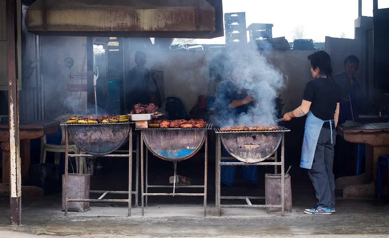 เตาปิ้งย่างสามเตาควันกรุ่นที่ร้านอาหารแห่งหนึ่งในแม่สะเรียง มีคนยืนย่างเนื้ออยู่ ภาพเพื่อแสดงบรรยากาศ ไม่ได้แนะนำร้านนี้ ภาพจาก Wikimedia Commons ผู้ถ่าย Takeaway สัญญา CC BY-SA 4.0