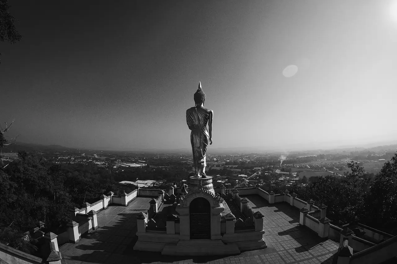 ภาพขาวดำของพระพุทธรูปบนลานชมวิวและตัวเมืองด้านล่าง ถ่ายเงยด้วยเลนส์มุมกว้าง มีแสงแฟลร์จากดวงอาทิตย์ที่มุมขวาบน ภาพจาก Wikimedia Commons ผู้ถ่าย Peerawat.b สัญญา CC BY-SA 4.0 ไม่ลงวันที่ถ่าย เป็นภาพประกอบ