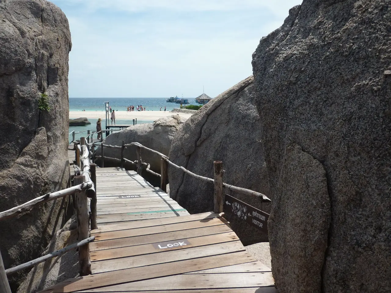 ทางไม้เลียบระหว่างก้อนหินใหญ่ ปลายทางเป็นชายหาดและน้ำทะเล ชื่อไฟล์บน Commons ว่าทางไปท่าเรือเกาะนางยวน เราไม่ได้ยืนยันจุดเอง ภาพของ Dirk Enthoven จาก Wikimedia Commons สัญญา CC BY 3.0