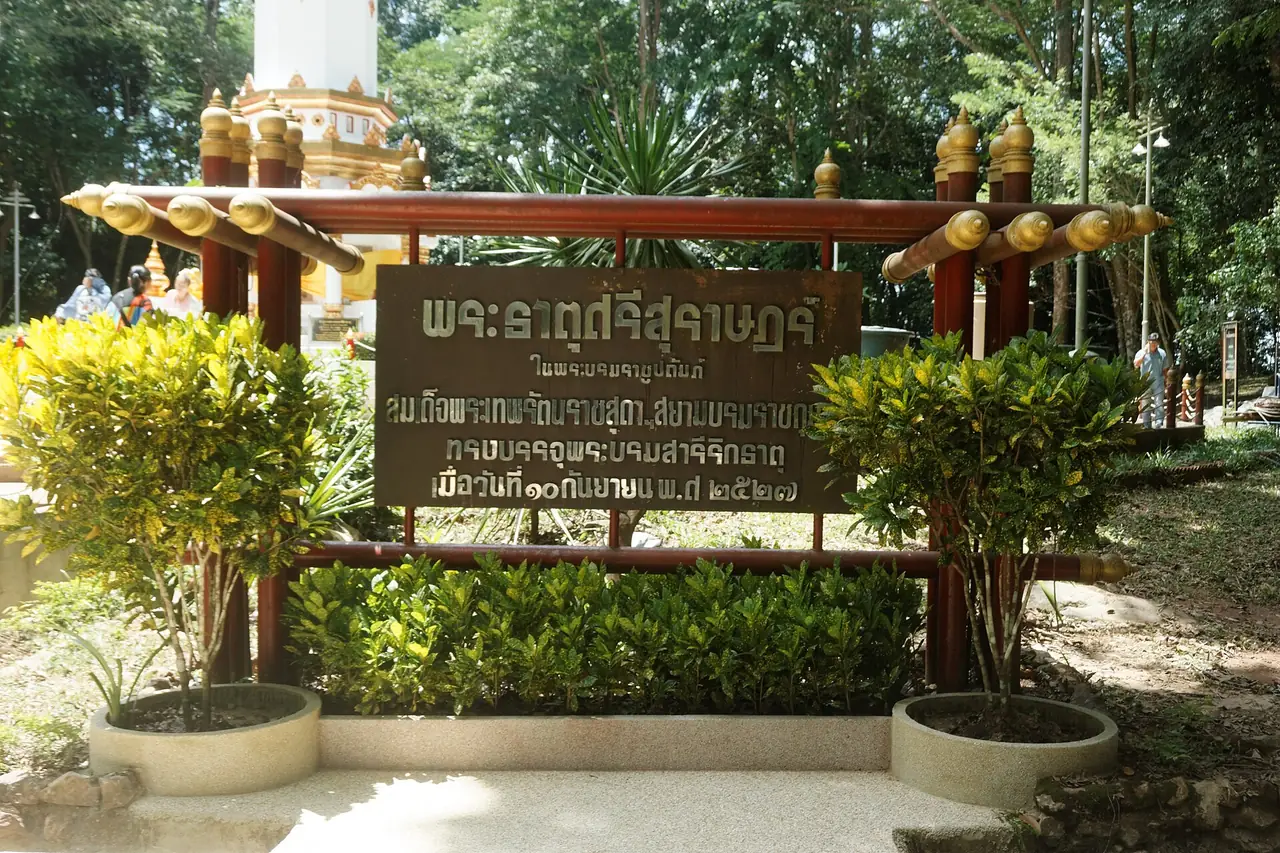 ป้ายชื่อพระธาตุศรีสุราษฎร์ที่เขาท่าเพชร มีข้อความตัวอักษรไทยและต้นไม้เล็กล้อมรอบ ภาพจาก Wikimedia Commons ผู้ถ่าย Ahoerstemeier สัญญา CC BY-SA 4.0 ไม่ระบุปีที่ถ่าย ข้อความบนป้ายในภาพมีวันที่ปี พ.ศ. 2527