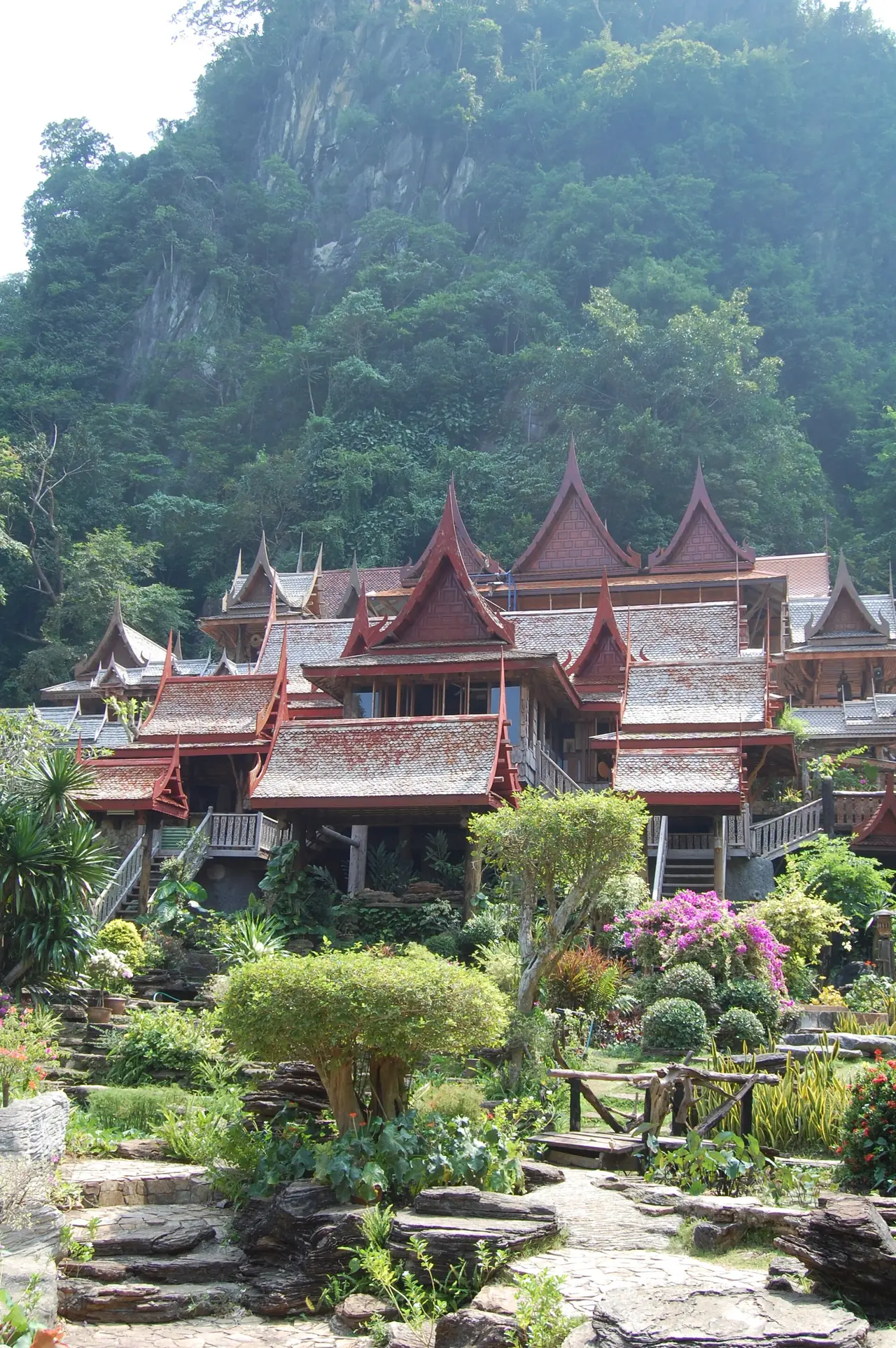 กลุ่มอาคารไม้หลังคาสีแดงซ้อนกันหลายชั้นใต้ภูเขาป่ารกเขียว ชื่อไฟล์ Wat Kao Wong04 Commons ระบุว่าเป็นวัดถ้ำเขาวง ใช้เป็นภาพบรรยากาศของพื้นที่บ้านไร่ ไม่ใช่ภาพฝายหรือวัดผาทั่ง ภาพจาก Wikimedia Commons ผู้ถ่าย Meneerke bloem สัญญา CC BY-SA 3.0 ไม่ทราบปีที่ถ่าย